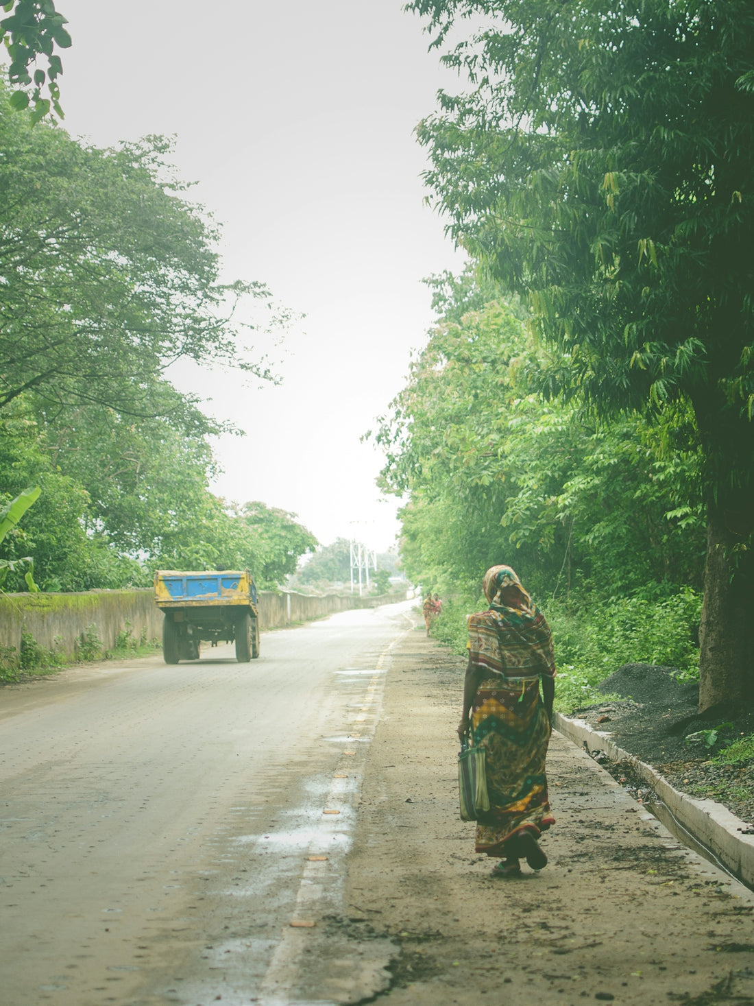 a woman walking down a dirt road next to a forest
