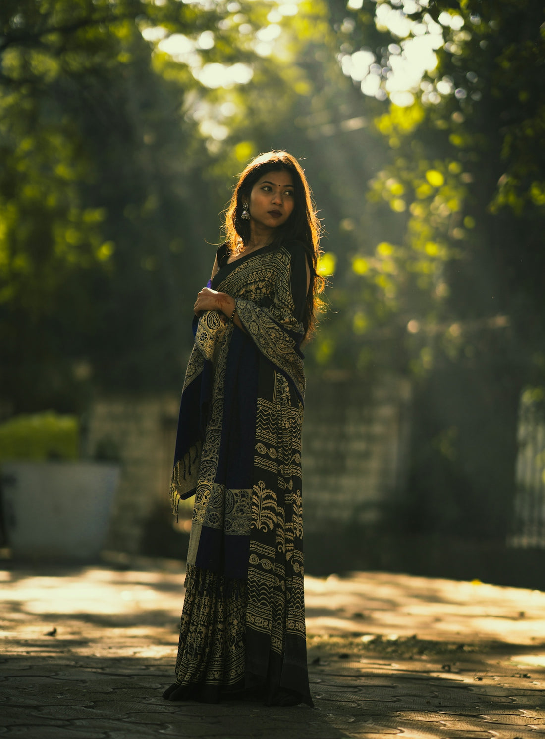 A young woman in a patterned sari stands outdoors.